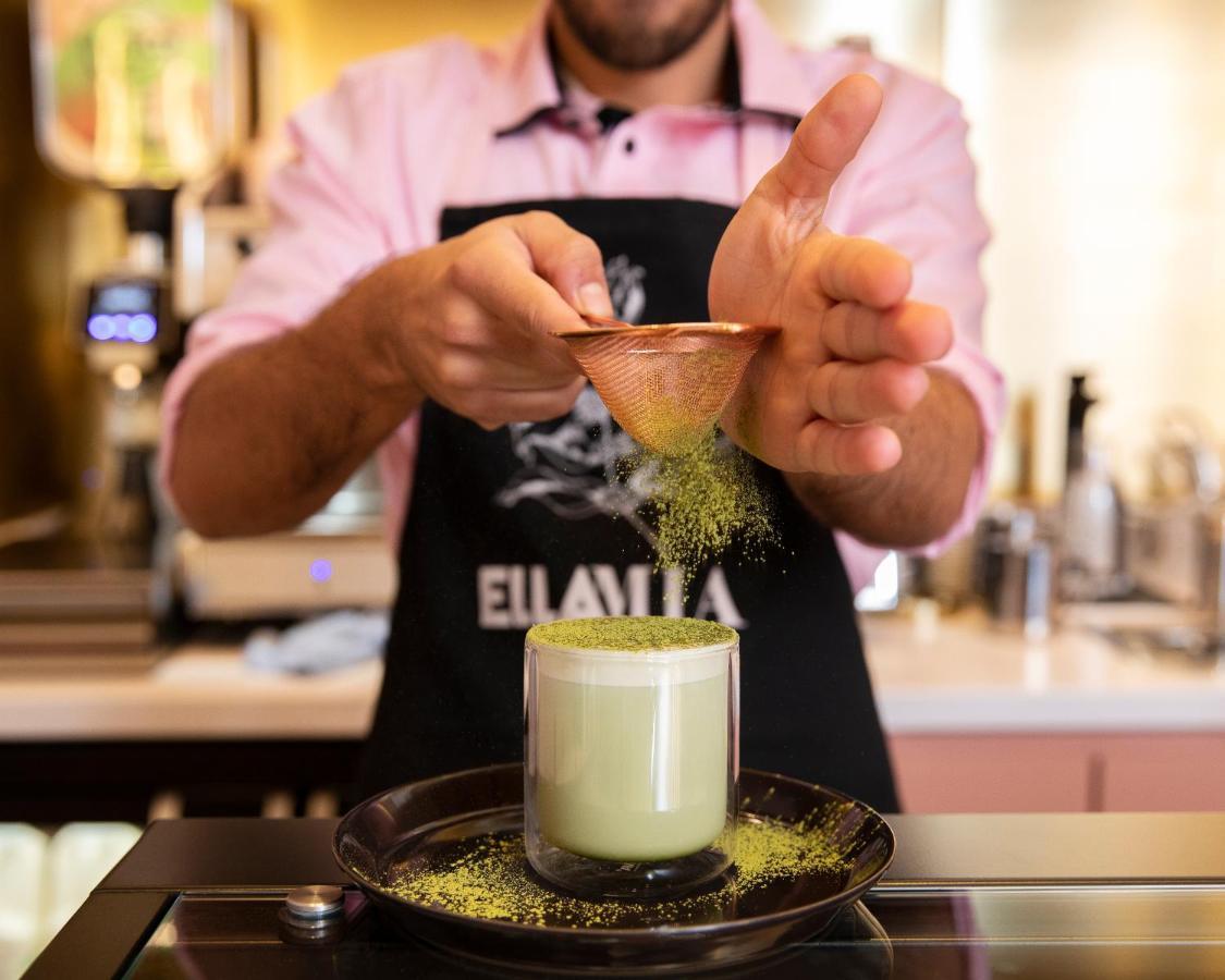 โรงแรมเซนต์ มาร์ติน เลน ลอนดอน ภายนอก รูปภาพ The image shows a person preparing a drink, likely a matcha-based beverage. They are wearing an apron and using a small scoop to sprinkle what appears to be green matcha powder into a glass. The glass is filled with a light green drink, possibly matc
