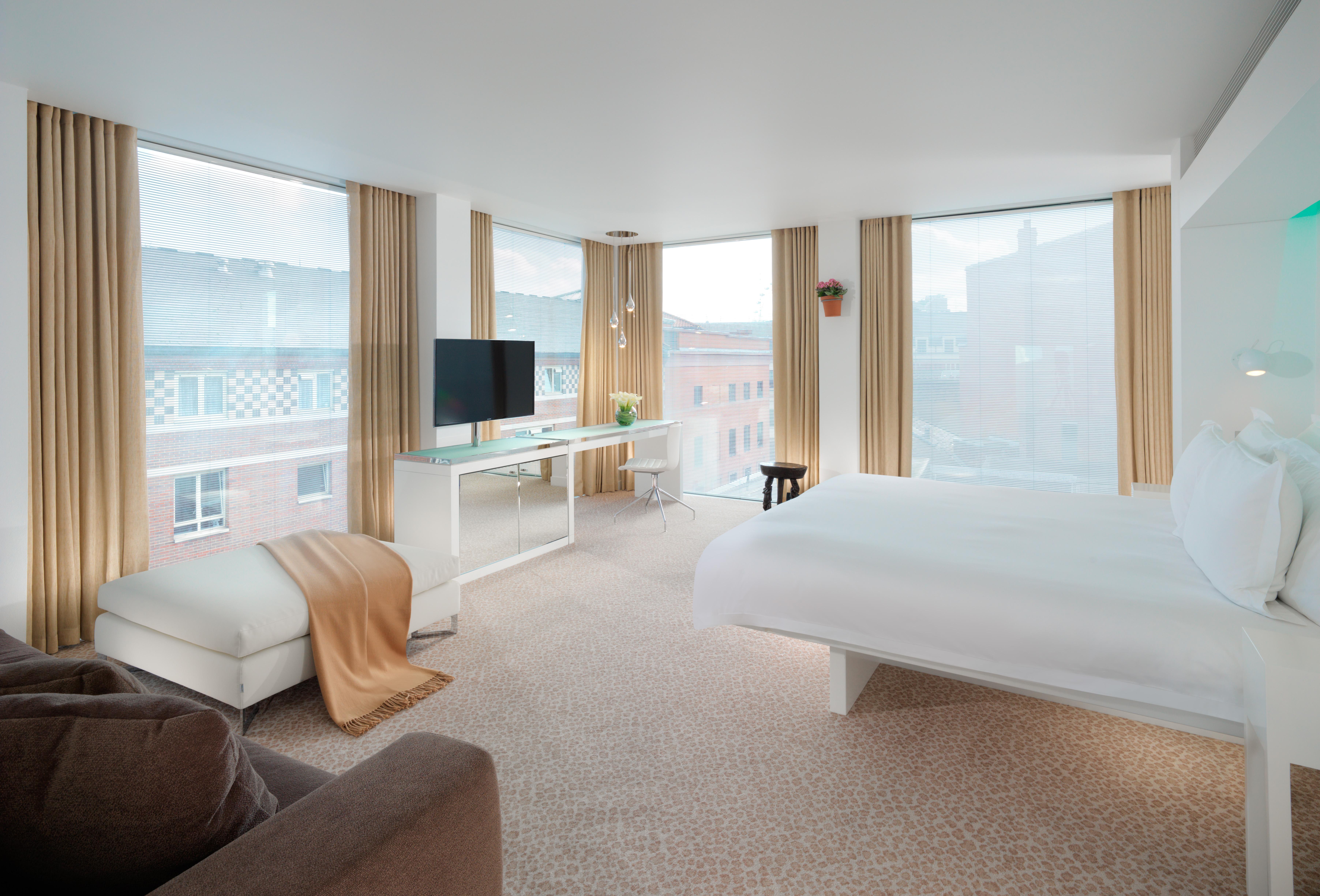 โรงแรมเซนต์ มาร์ติน เลน ลอนดอน ภายนอก รูปภาพ The photo displays a modern hotel room that features large windows allowing natural light to fill the space. The room includes a comfortable bed with white linens, a cozy chair and a throw blanket in neutral tones, and a small side table. There is a 