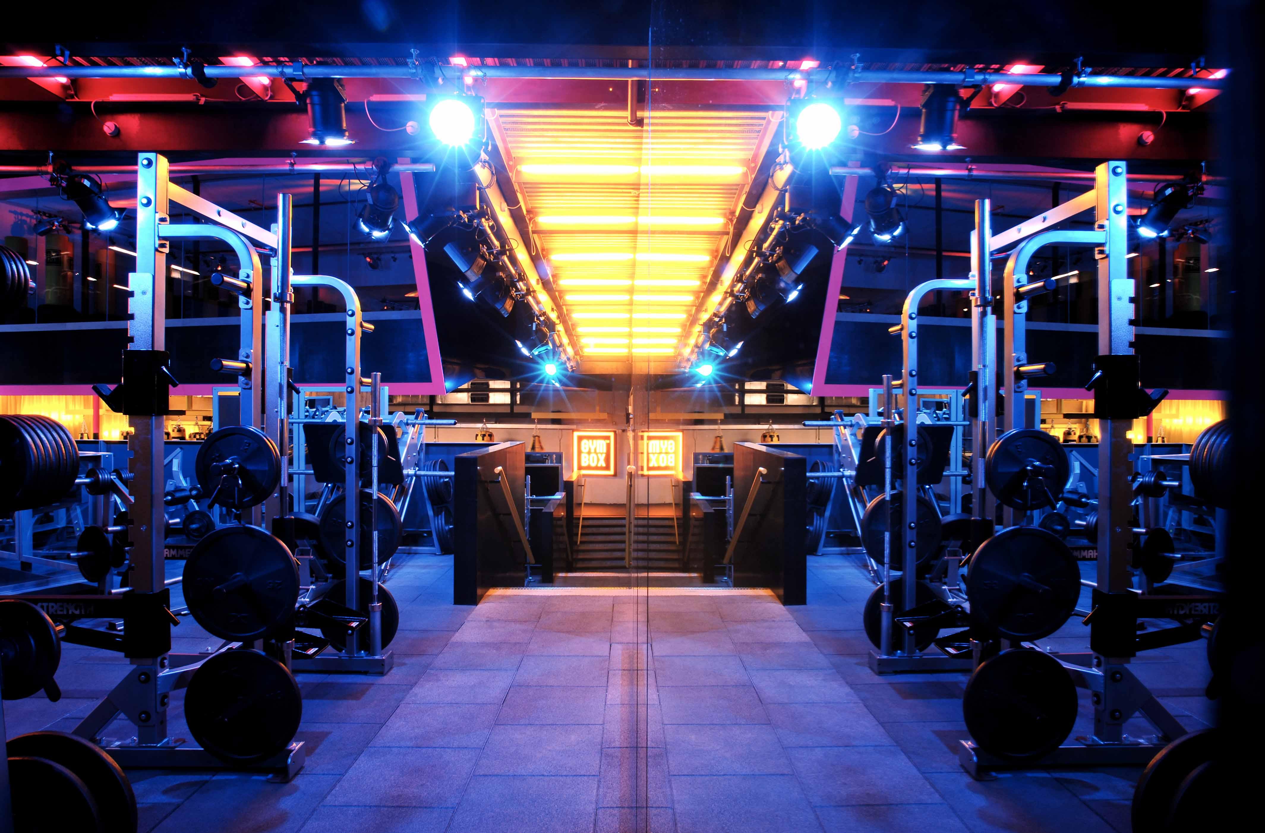 โรงแรมเซนต์ มาร์ติน เลน ลอนดอน ภายนอก รูปภาพ The photo depicts a modern gym interior, characterized by a brightly lit space with blue and orange lighting. In the foreground, there are multiple gym equipment setups, including weightlifting machines and benches. The gym features a sleek and conte