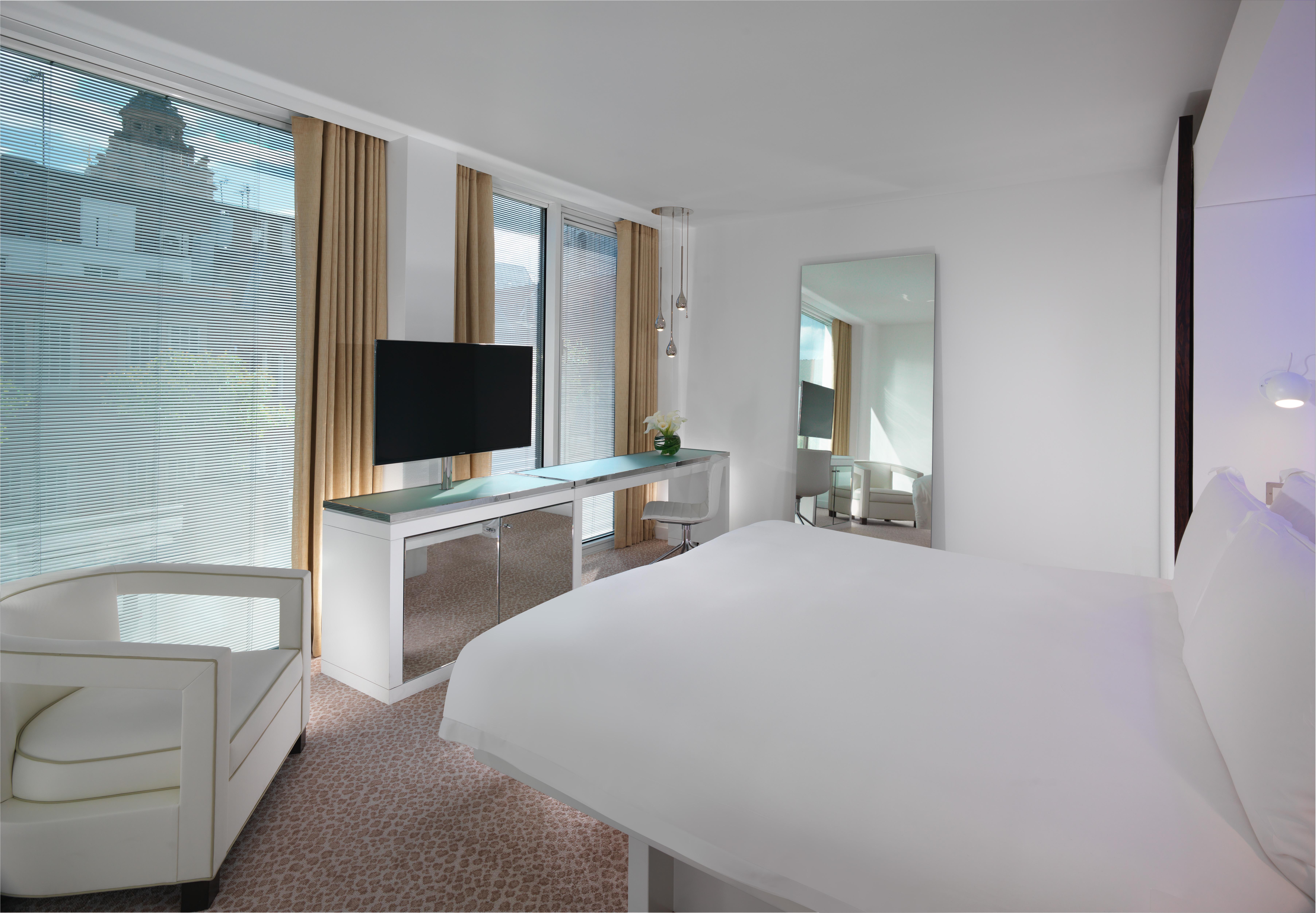 โรงแรมเซนต์ มาร์ติน เลน ลอนดอน ภายนอก รูปภาพ The photo shows a modern hotel room featuring a king-sized bed with white bedding. There is a sleek, minimalist design with light-colored walls and a carpeted floor. A large window allows natural light to fill the room, with sheer curtains providing 