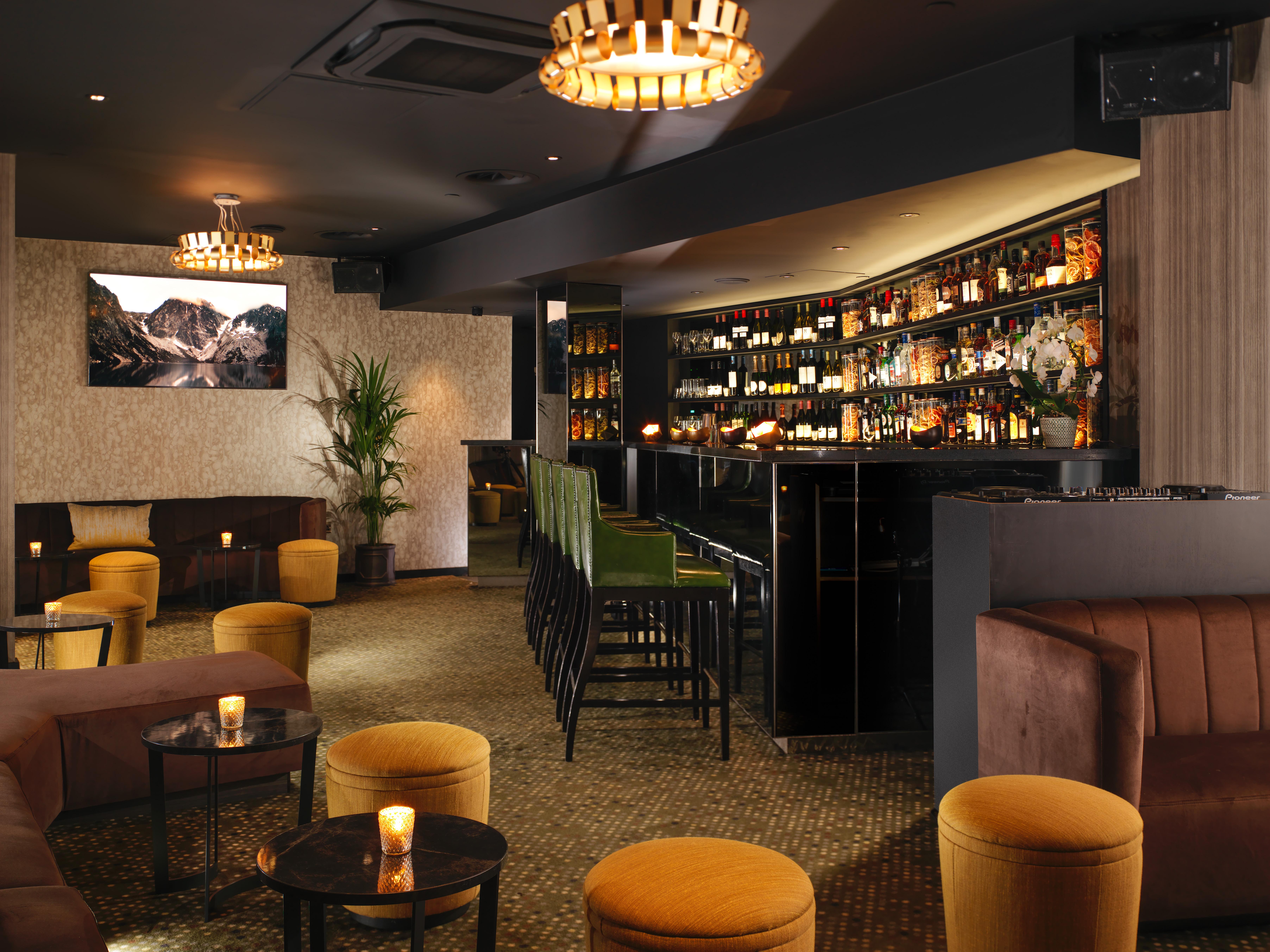 โรงแรมเซนต์ มาร์ติน เลน ลอนดอน ภายนอก รูปภาพ The photo depicts a stylish bar or lounge interior. The space features a dark, sophisticated color scheme with plush seating, including brown couches and vibrant yellow stools. A illuminated bar area is prominently displayed, lined with various bottl