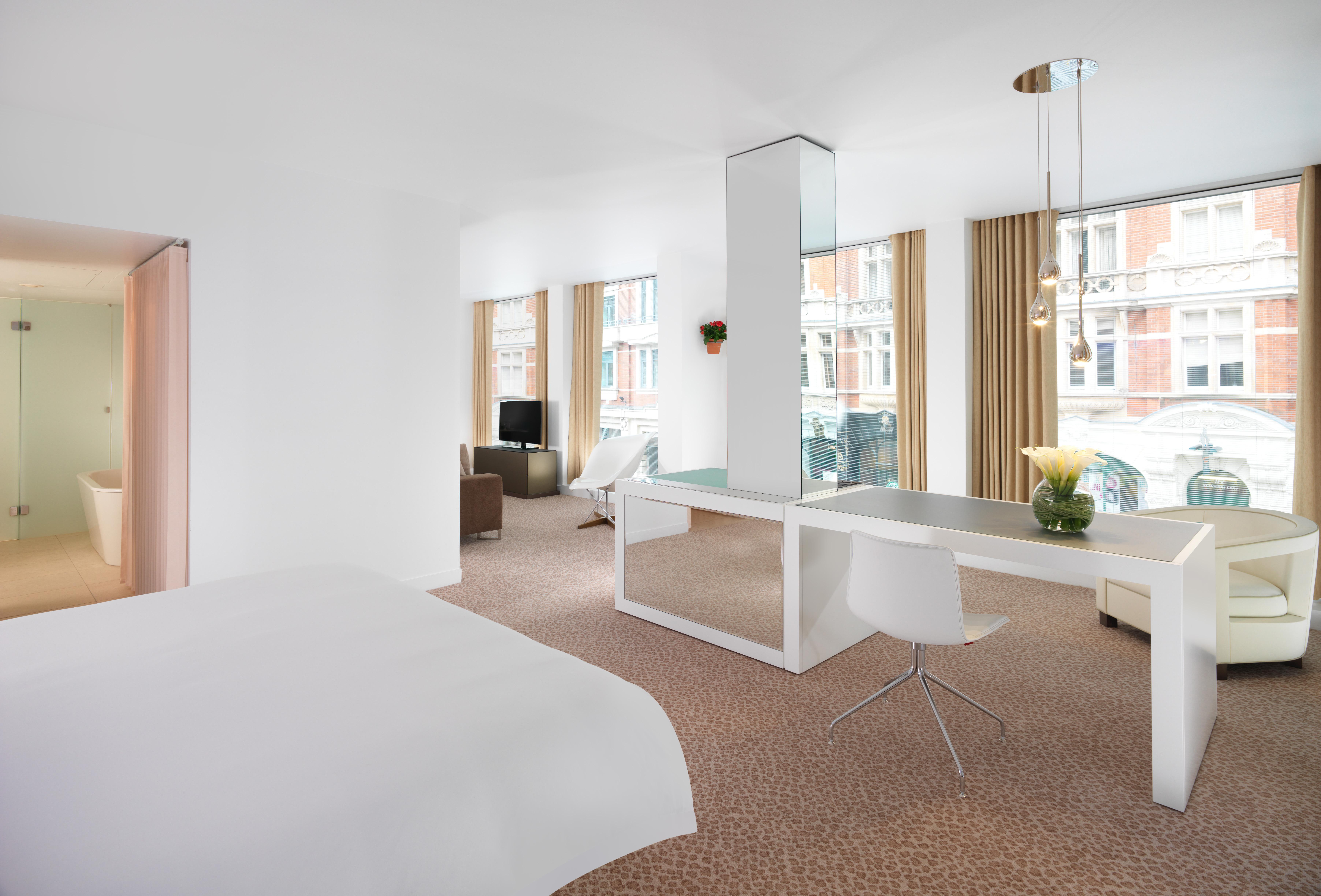 โรงแรมเซนต์ มาร์ติน เลน ลอนดอน ห้อง รูปภาพ The photo shows a modern hotel room with a bright, minimalist design. The room features large windows that allow natural light to fill the space. There is a bed with a white duvet in the foreground, and in the background, you can see a workstation wi