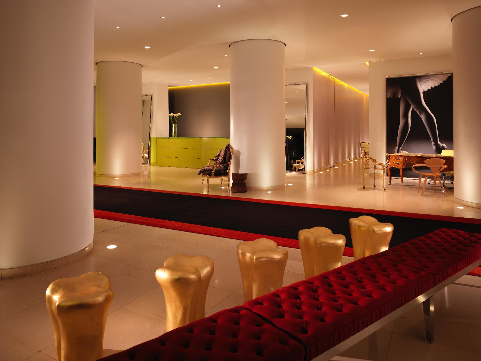 โรงแรมเซนต์ มาร์ติน เลน ลอนดอน ภายนอก รูปภาพ The photo shows a modern and stylish interior space, possibly a lobby or a lounge area. It features sleek white pillars and a polished floor, illuminated by soft ambient lighting. On one side, there is a green seating area, while on the opposite side