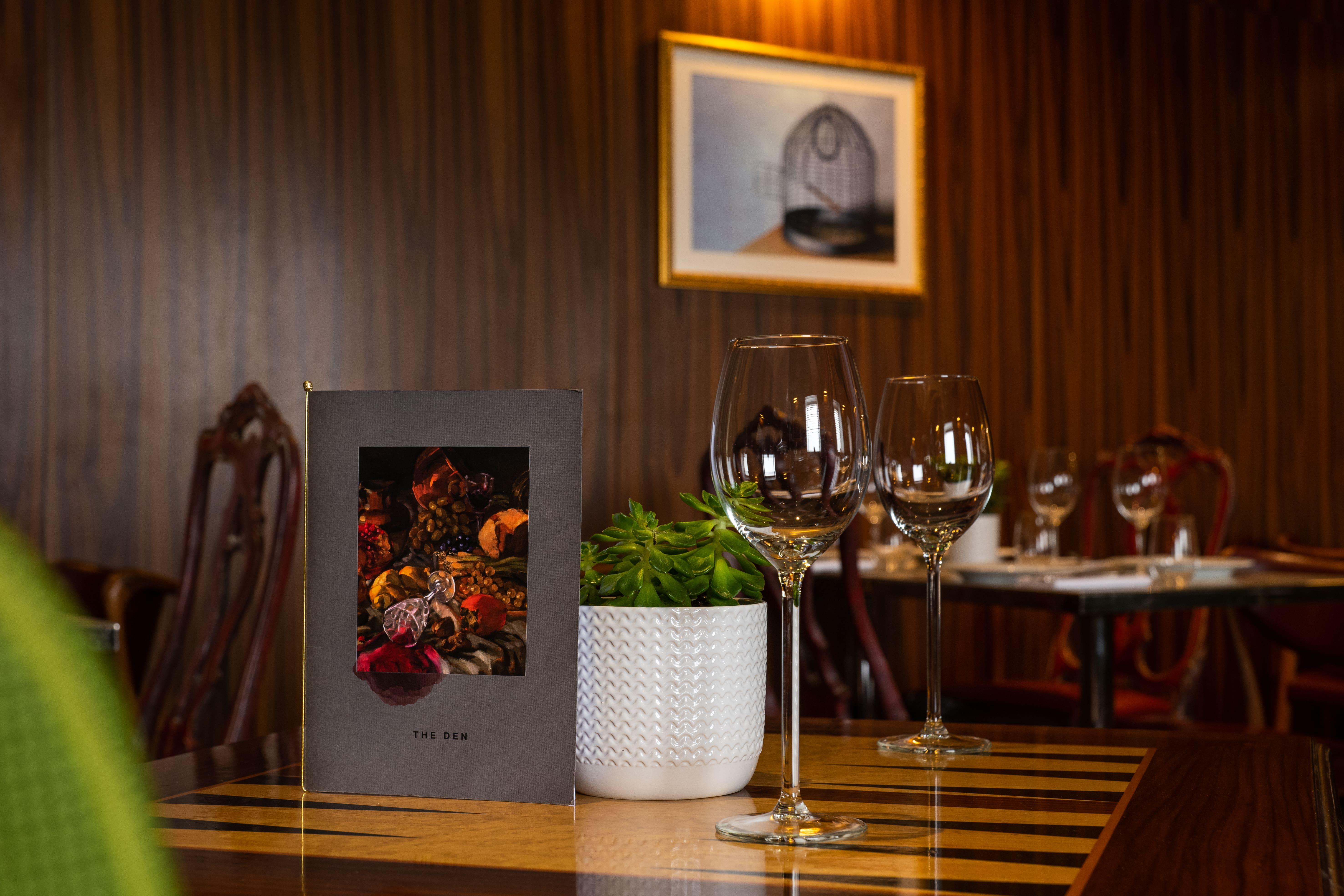โรงแรมเซนต์ มาร์ติน เลน ลอนดอน ภายนอก รูปภาพ The photo shows a cozy dining setting in a restaurant. A menu is prominently displayed on the table, featuring a colorful design that includes images of spices or garnishes. Next to the menu, there are two elegant wine glasses, reflecting the ambianc