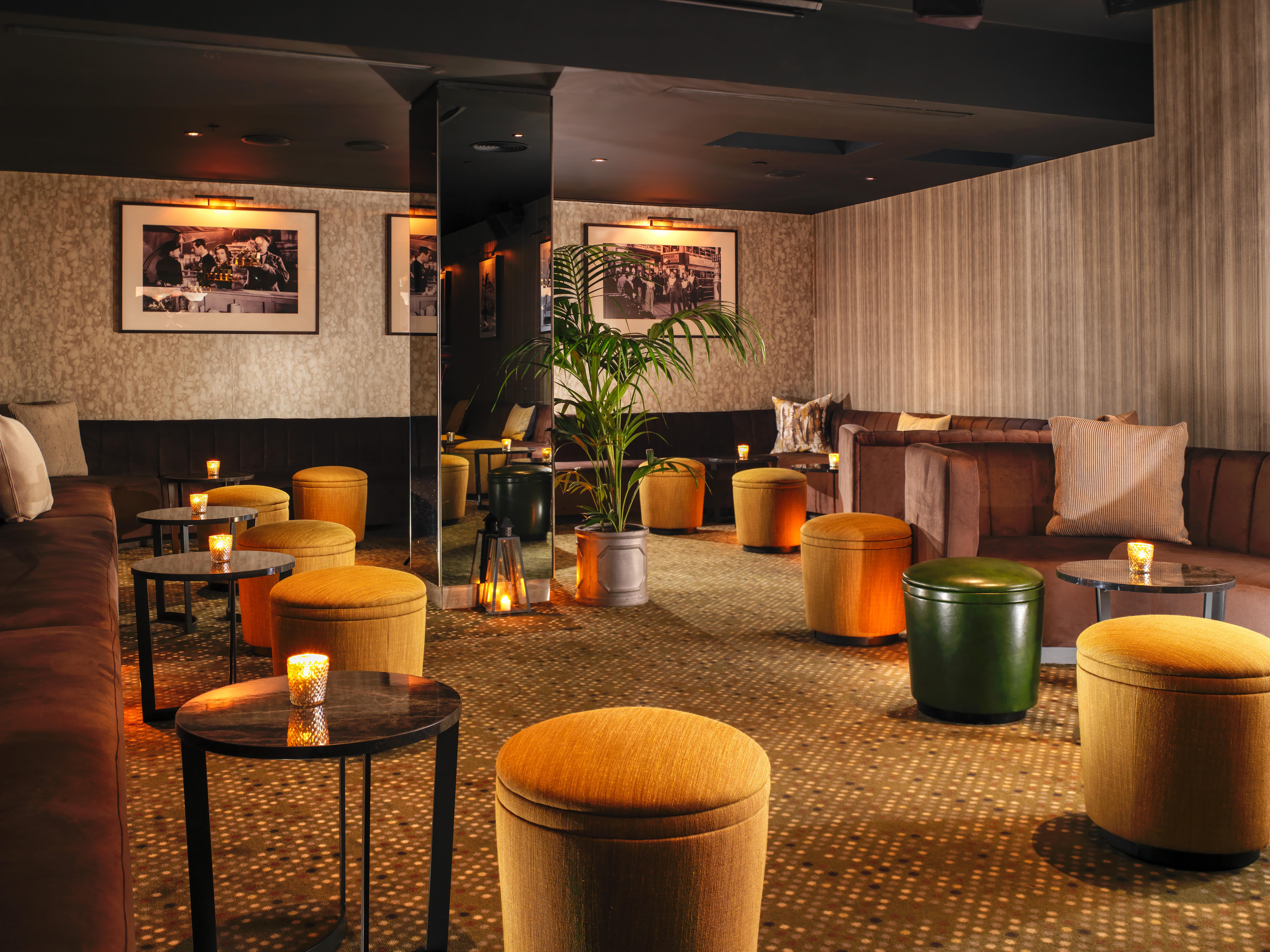 โรงแรมเซนต์ มาร์ติน เลน ลอนดอน ภายนอก รูปภาพ The photo shows a cozy lounge area with a warm and inviting atmosphere. The space features a mix of seating arrangements, including cushioned benches and small round tables. There are several colorful ottomans, predominantly in shades of yellow and g