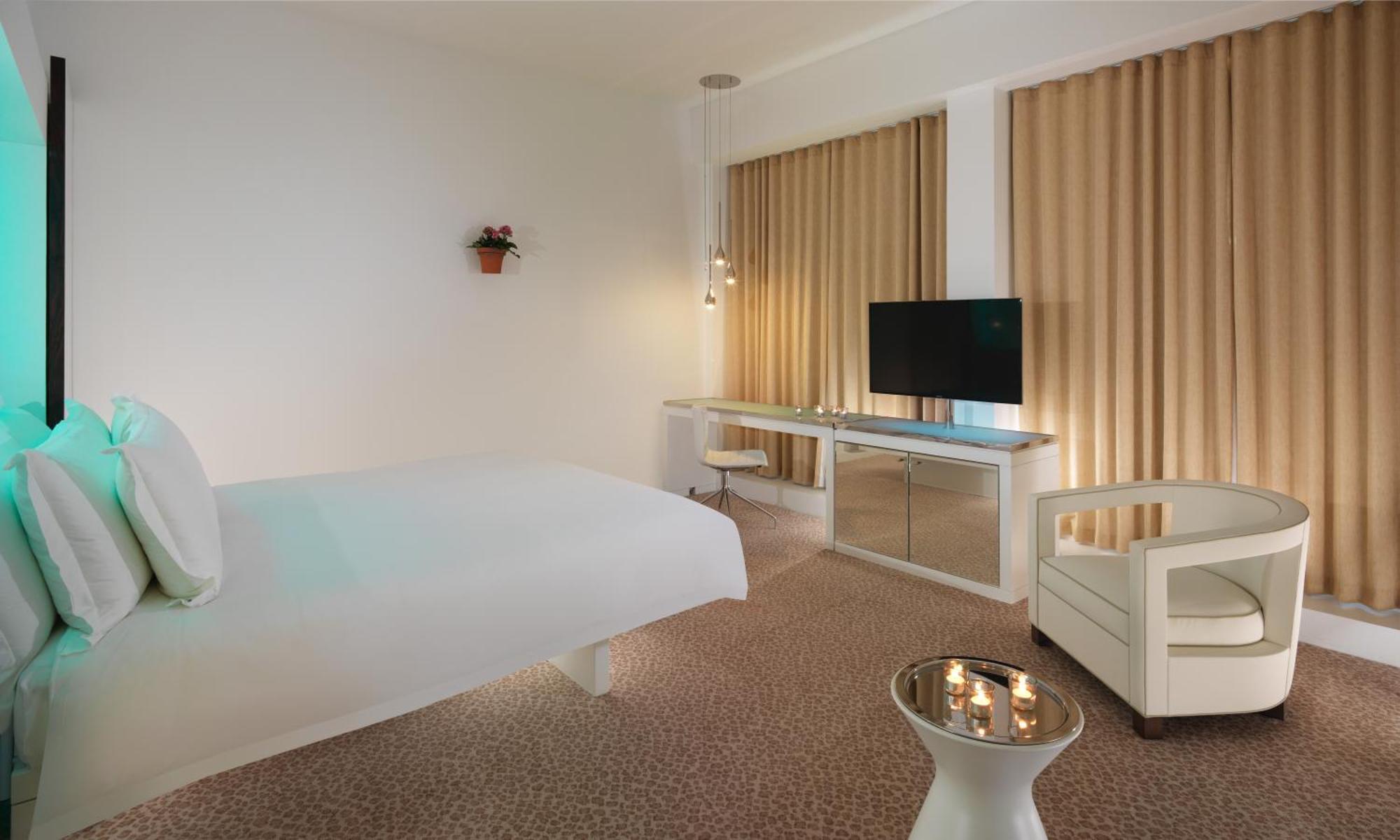 โรงแรมเซนต์ มาร์ติน เลน ลอนดอน ภายนอก รูปภาพ The photo shows a modern hotel room with a minimalist design. It features a large bed against one wall, a flat-screen TV mounted on another wall, and a contemporary desk with a mirror. Large windows are dressed with light-colored curtains, allowing n