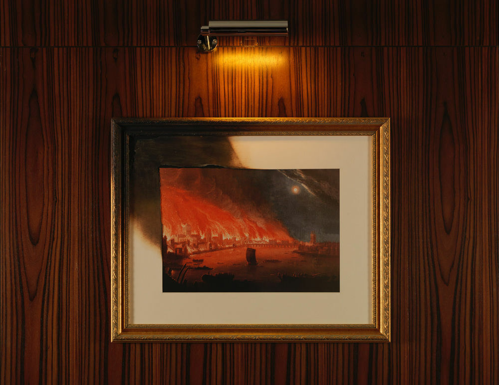 โรงแรมเซนต์ มาร์ติน เลน ลอนดอน ภายนอก รูปภาพ The photo shows a framed painting illuminated by a small light above it. The artwork depicts a dramatic scene with fiery red and orange hues, suggesting a sense of destruction or chaos. The painting is set against a wall with a wood grain texture, an
